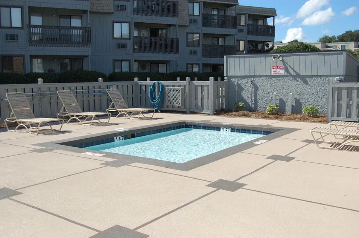 An inviting scene showing a sparkling swimming pool surrounded by lounge chairs and a safe fenced area, perfect for relaxing or socializing with family after a day on the beach.