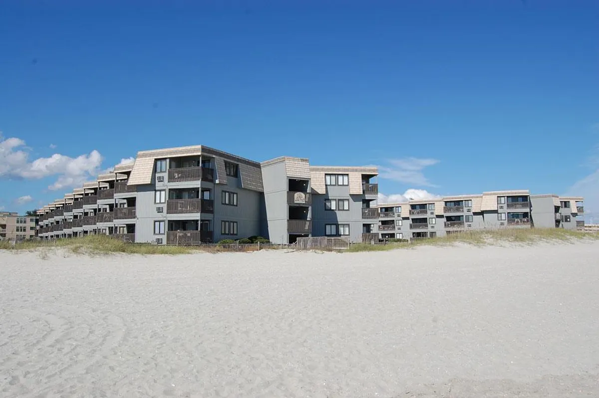 A modern beachfront building with expansive, private balconies overlooking the ocean. The image clearly showcases the balconies as key features, highlighting the proximity to the beach and the relaxing, open-air vibe associated with coastal living.