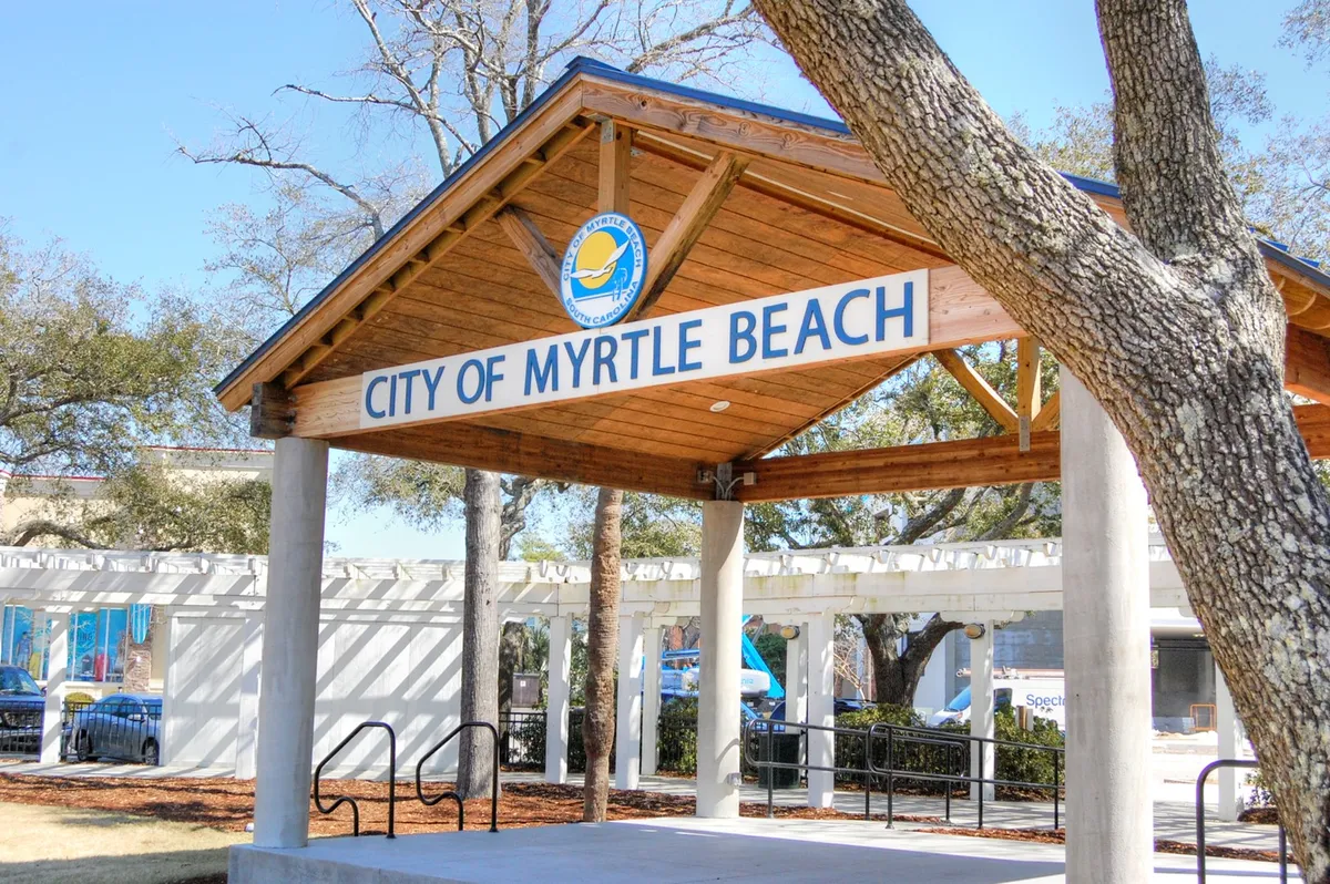 A friendly exterior view of a city pavilion surrounded by trees, featuring a prominent city sign. The open-air structure hints at community gatherings and local events, suggesting an inviting environment perfect for discovering the area's culture and seasonal happenings.