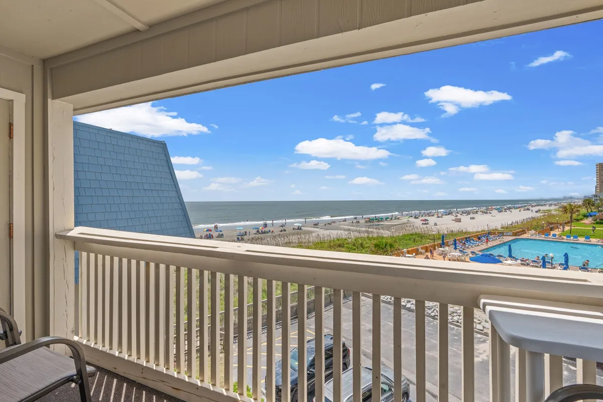 A sweeping view encompassing the ocean, sandy beach, swimming pool, and scattered clouds above. There is a sense of openness and tranquility, with the beach and ocean inviting relaxation and the pool area suggesting an additional leisure space.