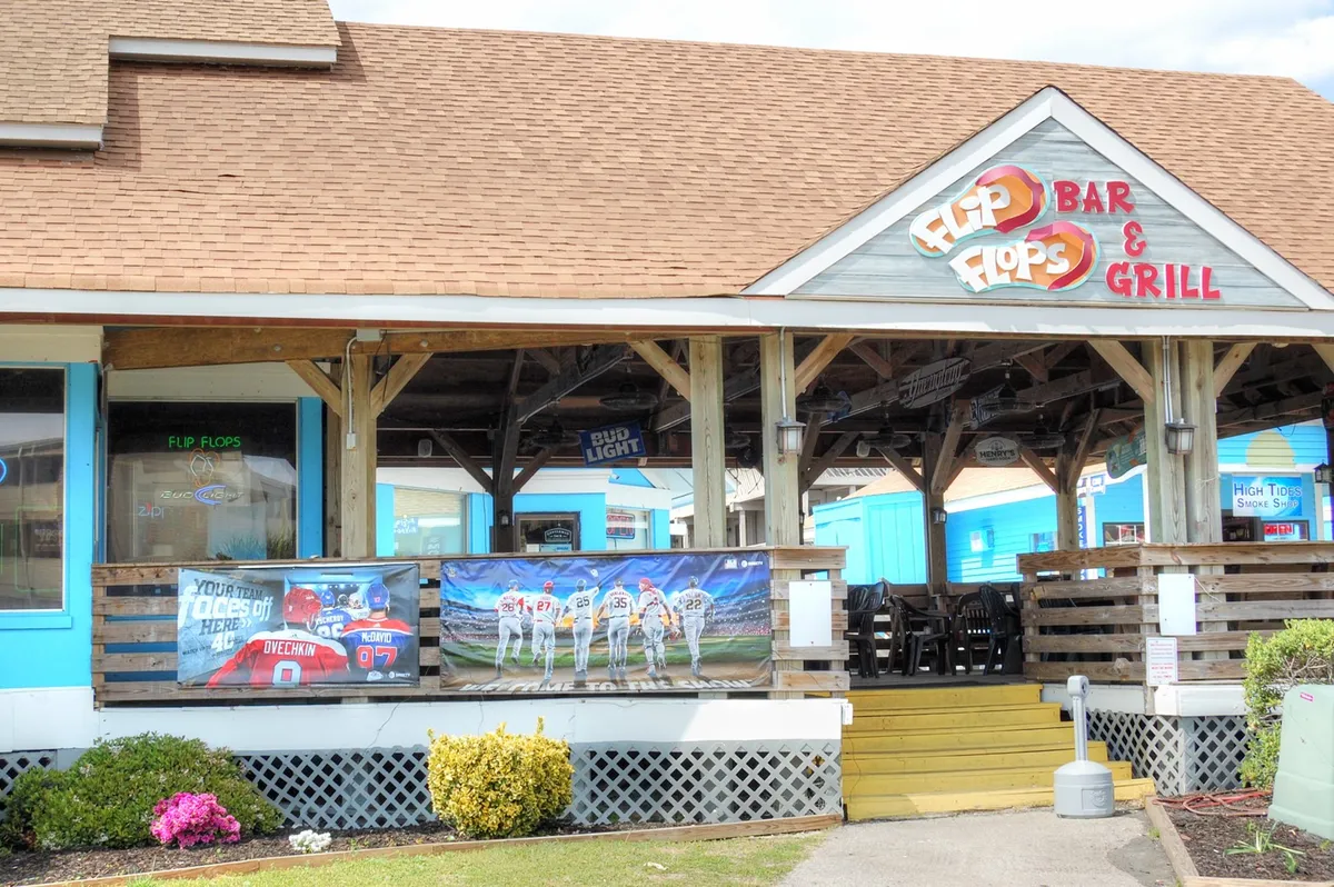 This exterior image captures the inviting entrance to 'Flip Flops Bar & Grill,' featuring vibrant signage, colorful banners, and an outdoor seating area. The lively ambiance hints at a popular spot for socializing, dining, and enjoying the Myrtle Beach nightlife.